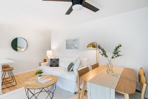 Ein modernes Wohnzimmer mit einem weißen Sofa, einem runden Couchtisch und einem Esstisch mit Stühlen.