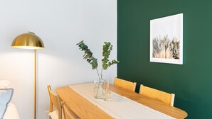 Ein Essbereich mit einem Holztisch, Stühlen, einer klaren Vase mit Grünpflanzen, einer Stehlampe und einem gerahmten Kunstwerk an der Wand.