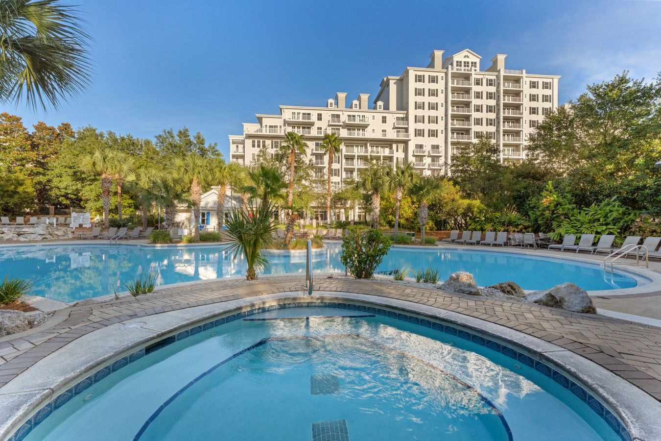 A hotel with a swimming pool surrounded by lounge chairs and palm trees.