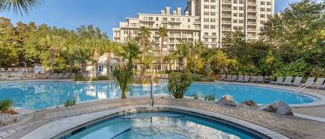 Un hotel con piscina rodeada de sillones de descanso y palmeras.