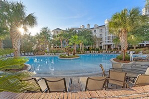 A swimming pool with lounge chairs and palm trees, surrounded by a building with a classical architectural style.
