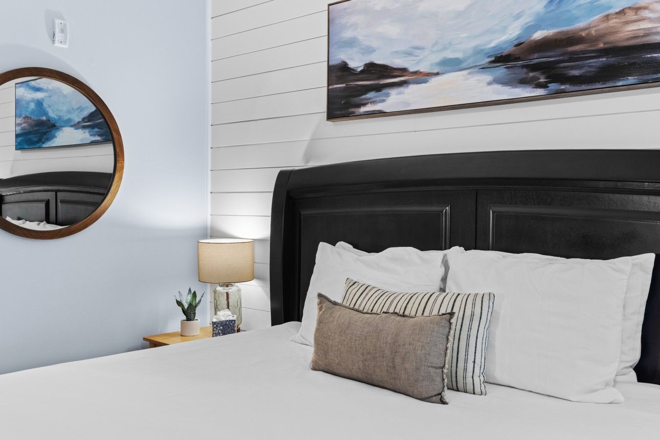 Et hotelværelse med en seng, et natbord med lampe, et spejl og et billede på væggen.