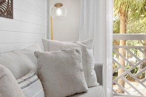 A white wooden wall with a decorative panel, a clear glass pendant light, and a view of palm trees through a white lattice window.