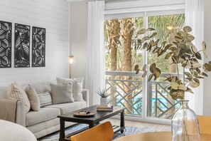 A modern living room with a sofa, coffee table, and a view of palm trees through large windows. - 🌴 Stylish Studio Retreat in Sandestin Resort (Miramar Beach)
