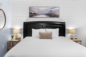 A hotel room with a large bed, two bedside tables with lamps, a wall-mounted painting, and a round mirror.