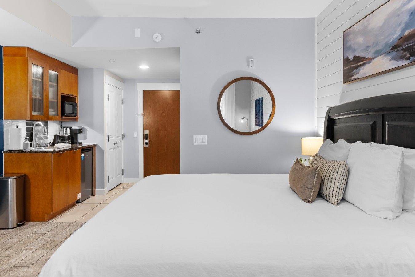Ein Hotelzimmer mit einem großen Bett, einem Holzschrank, einer Küchenzeile und einem runden Spiegel an der Wand.