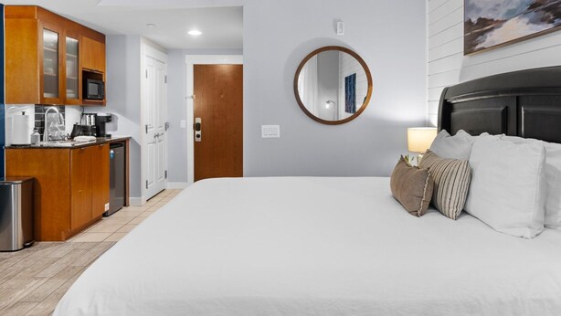 A hotel room with a large bed, a wooden wardrobe, a kitchen area, and a round mirror on the wall. - 🌴 Stylish Studio Retreat in Sandestin Resort (Miramar Beach)