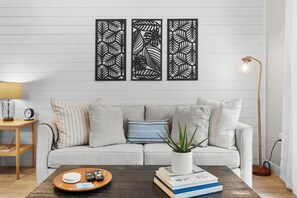 A living room with a sofa, a coffee table with books and a plant, a lamp, and a wall with three decorative panels.