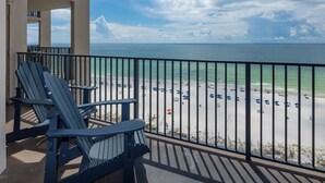 A balcony with Adirondack chairs overlooking a beach with umbrellas and people.