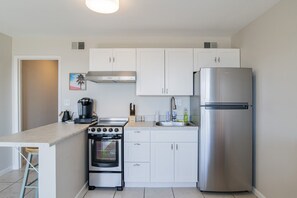 A compact kitchen with white cabinets, a stainless steel refrigerator, a built-in oven, and a coffee maker. - 🌊 Beachfront Bliss on the Fort Morgan Peninsula – Chic Condo with Panoramic Gulf Views (Gulf Shores)