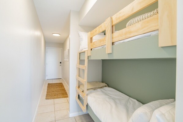 A bunk bed room with a ladder, a door, and a small rug on the floor.