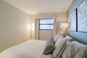 Une chambre d’hôtel avec un lit, une table de chevet avec une lampe, une fenêtre avec des rideaux et des œuvres d’art murales.
