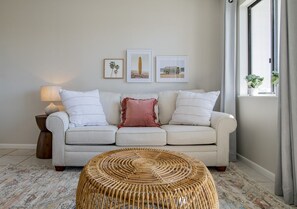 A living room with a sofa, a round woven coffee table, and framed pictures on the wall.