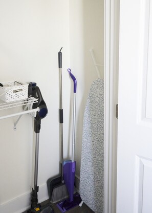 A laundry area with a drying rack, a vacuum cleaner, and a broom.