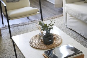 A living room with a white sofa, a coffee table with a woven placemat, a vase with green plants, and a book titled 'CHANEL COLLECTIONS'. - ✨ Stylish Beach Condo – Sleeps 6 in family friendly Gulf Place, Santa Rosa Beach (Santa Rosa Beach)