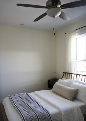 Ein Schlafzimmer mit einem Bett, einem Nachttisch, einem Deckenventilator und einem Fenster mit Vorhängen.