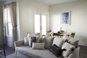 Un salon avec un canapé, une table à manger avec des chaises et une fenêtre avec des rideaux.