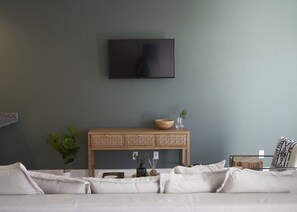 Ein modernes Wohnzimmer mit einem flachbildfernseher an der Wand, einem hölzernen Konsolentisch mit Dekoration und einem Sofa mit Kissen.