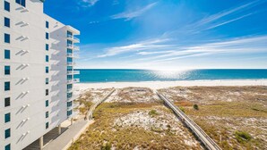 A modern hotel with a beach view, featuring a white facade, multiple balconies, and a pathway leading to the beach.