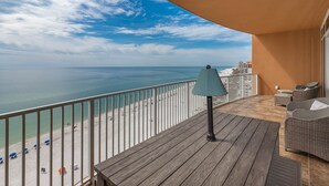 A balcony with a view of the beach, a table, and a lamp. - Phoenix Orange Beach 1005 3 Bedroom Condo (Orange Beach)
