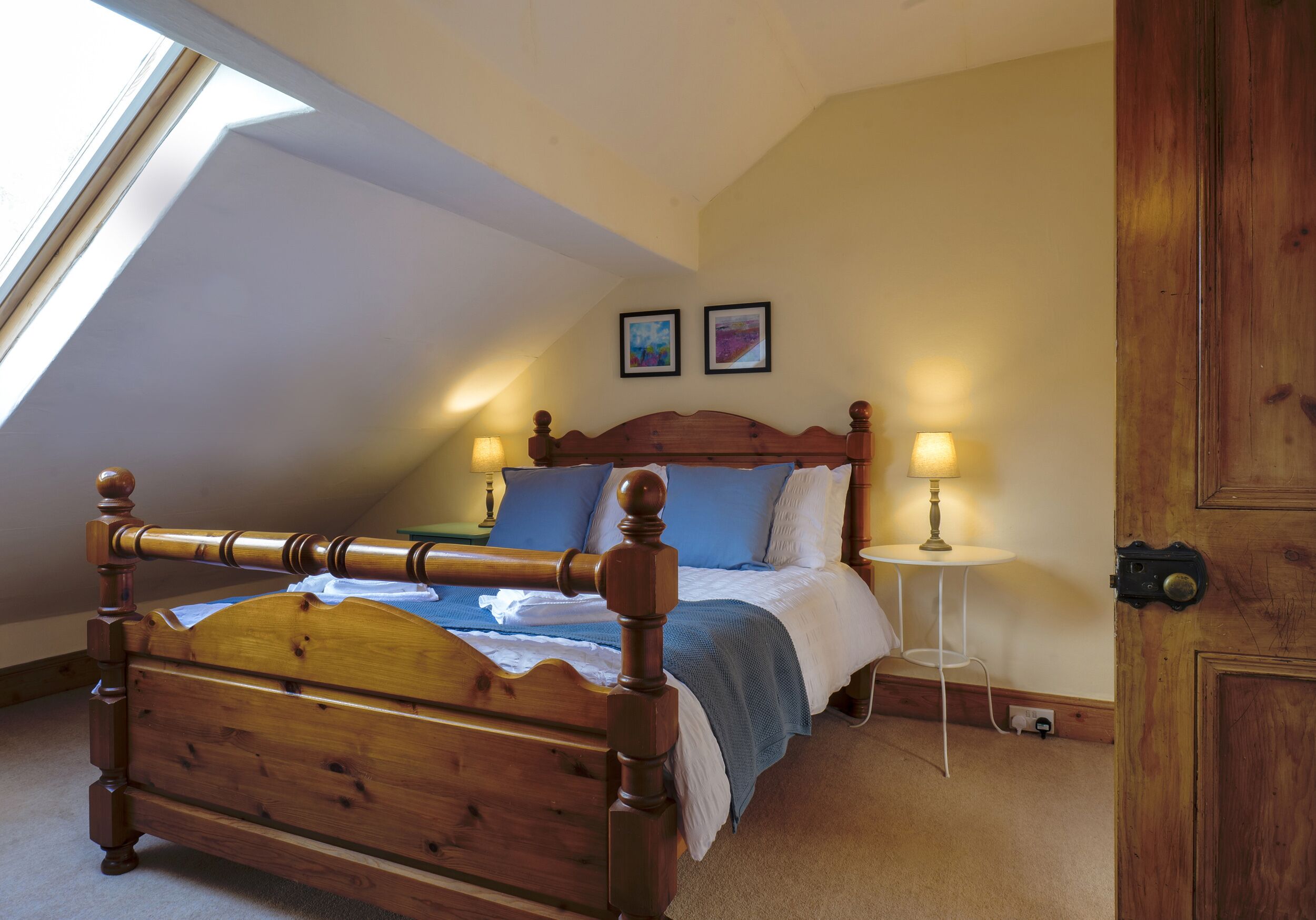 Quarto com cama de madeira, uma pequena mesa de cabeceira e uma janela.