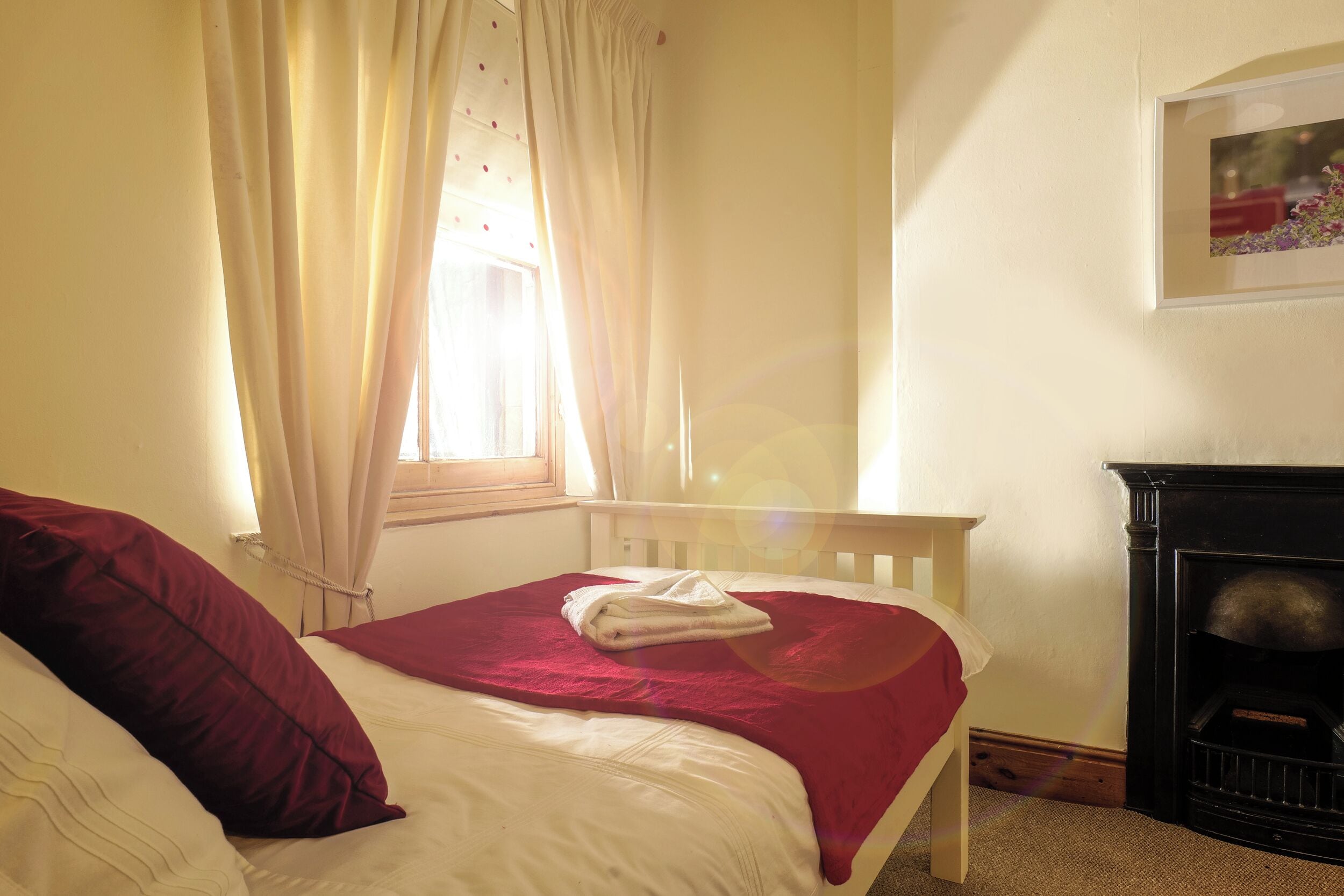 Quarto com cama, janela com cortinas, lareira e um quadro na parede.
