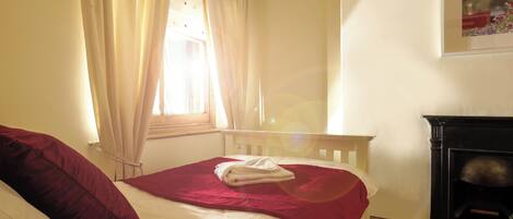 Quarto com cama, janela com cortinas, lareira e um quadro na parede.