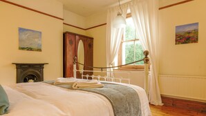 Un dormitorio con una cama, un aparador de madera, una chimenea y dos cuadros en las paredes.