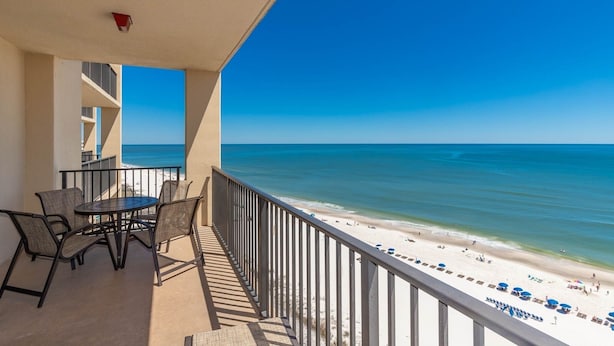 Ein Balkon mit Tisch und Stühlen mit Blick auf einen Strand.