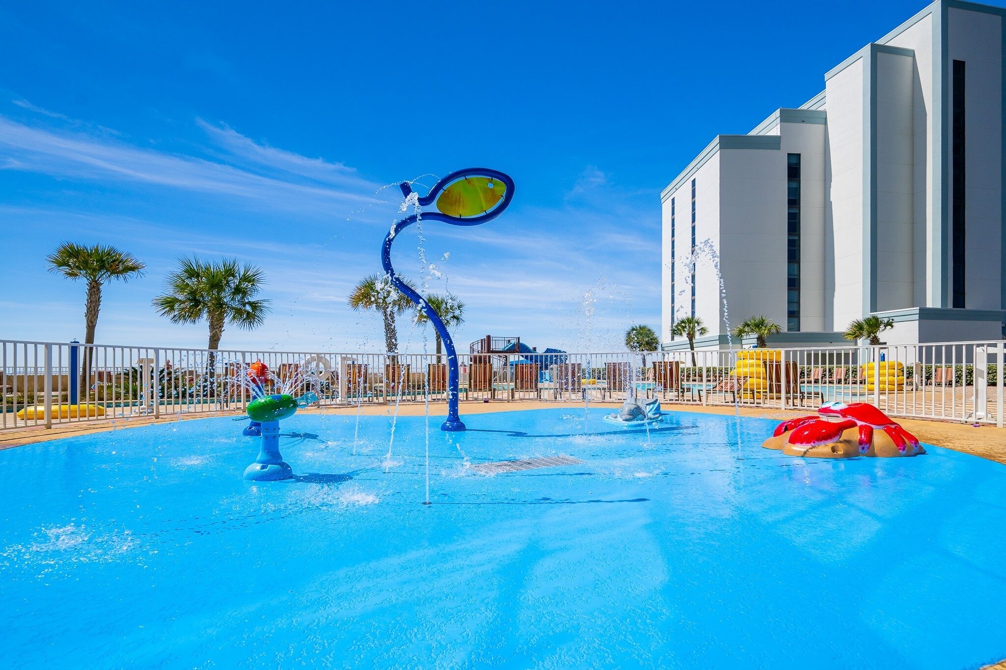 A swimming pool with water features, palm trees, and a building in the background.