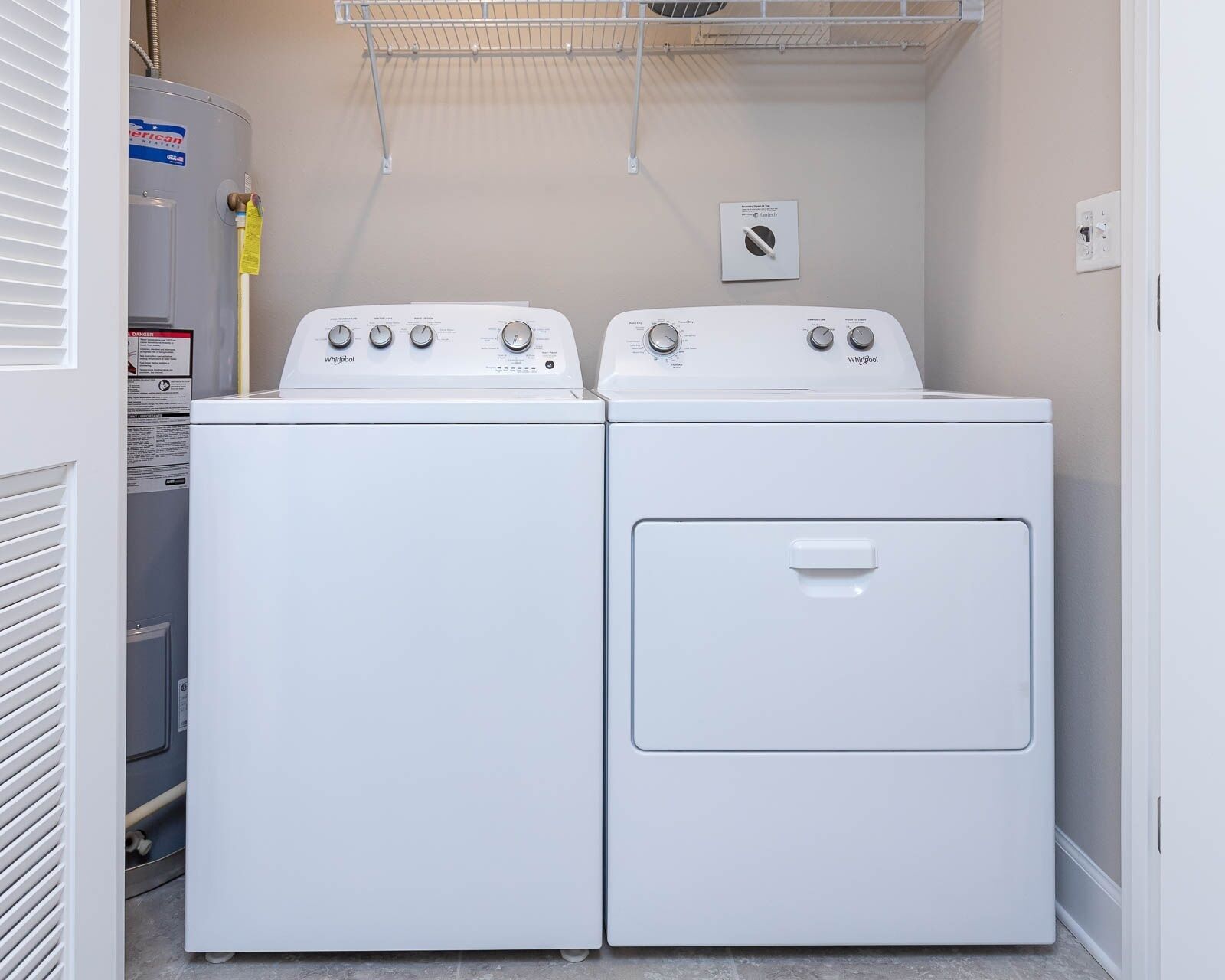 A laundry room with two stacked washers and a dryer, a water heater, and a utility meter on the wall.