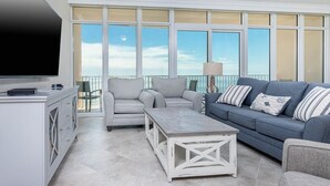 A spacious balcony with a view of the sea, furnished with a grey sofa, two armchairs, and a coffee table.