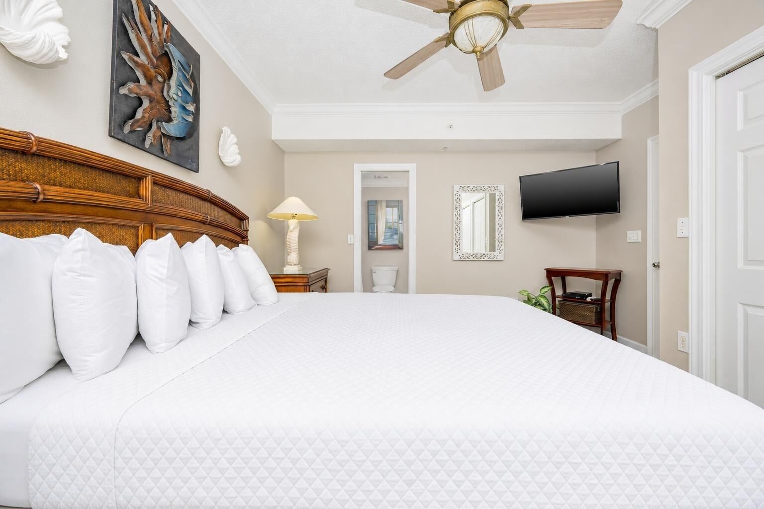 A hotel room with a large bed, a ceiling fan, a TV, and a door.