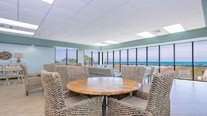 A spacious room with a round table and wicker chairs, large windows with a view of the ocean, and a ceiling with recessed lighting. - Phoenix East 108 1 Bedroom Condo (Orange Beach)