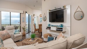 A spacious living room with a large TV, comfortable seating, and a balcony with a view. - Phoenix East 108 1 Bedroom Condo (Orange Beach)