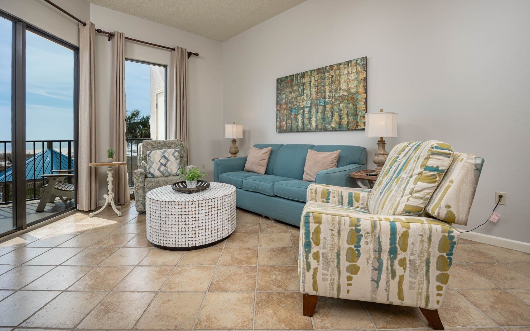 A living room with a blue sofa, a patterned armchair, a round coffee table, and a painting on the wall.