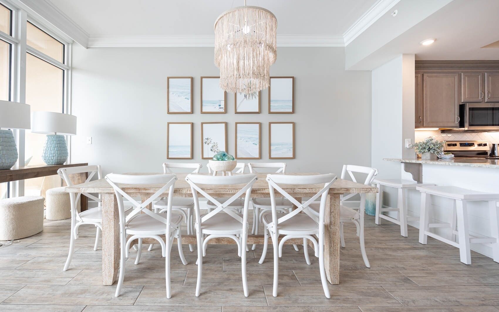 A dining area with a wooden table and white chairs, a chandelier, and framed pictures on the wall.