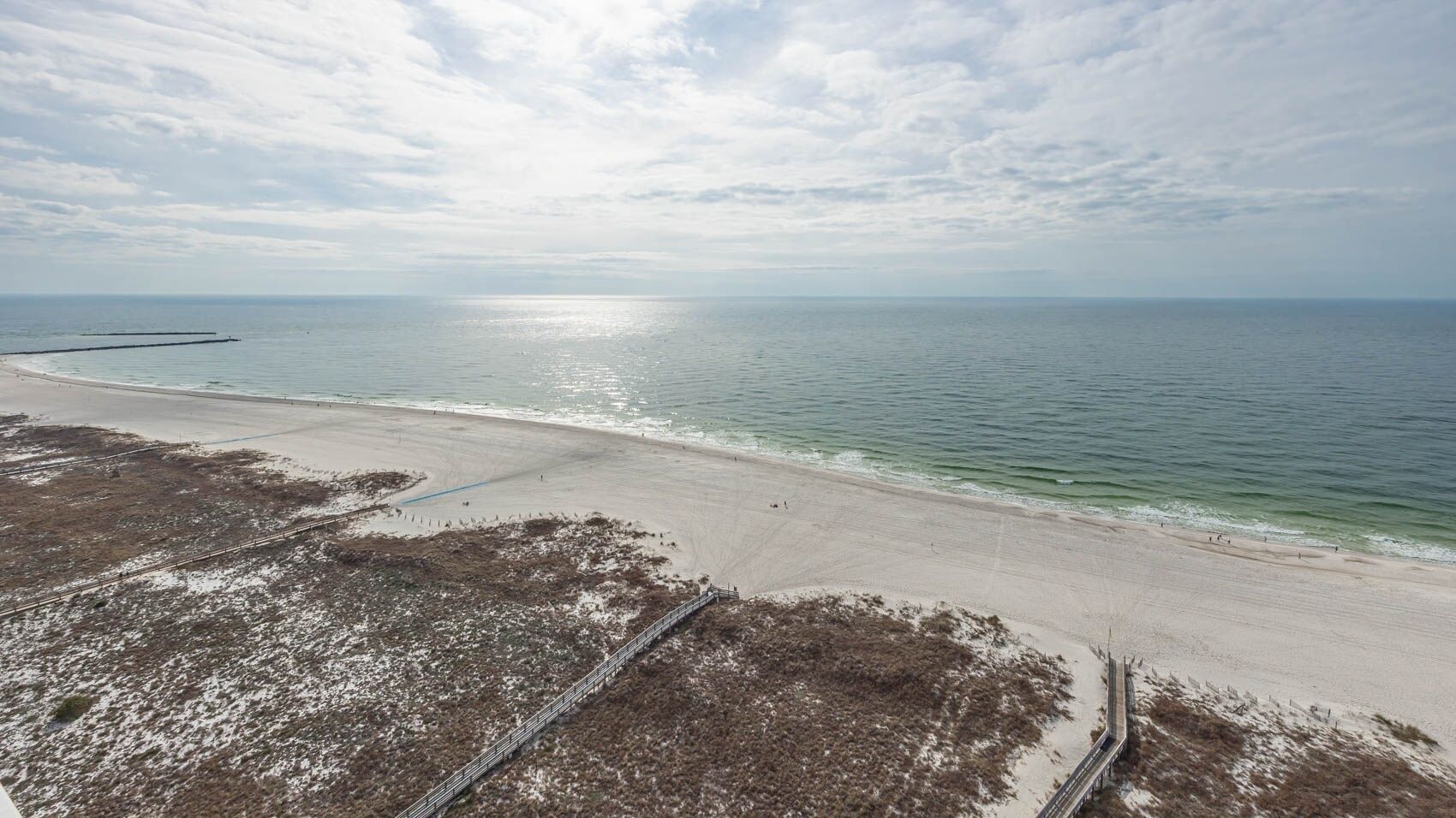 A beach with a sandy shore, a metal fence, and a clear view of the ocean.