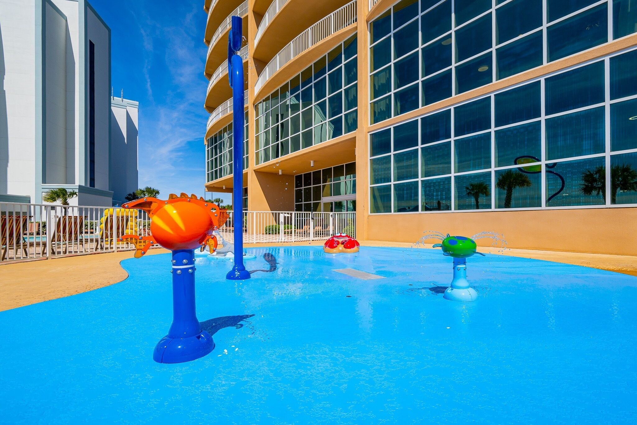 A water park area with play structures, a pool, and a building with large windows.