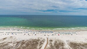 Uma praia com fileiras de guarda-sóis e cadeiras de praia, uma faixa de areia e o oceano ao fundo.