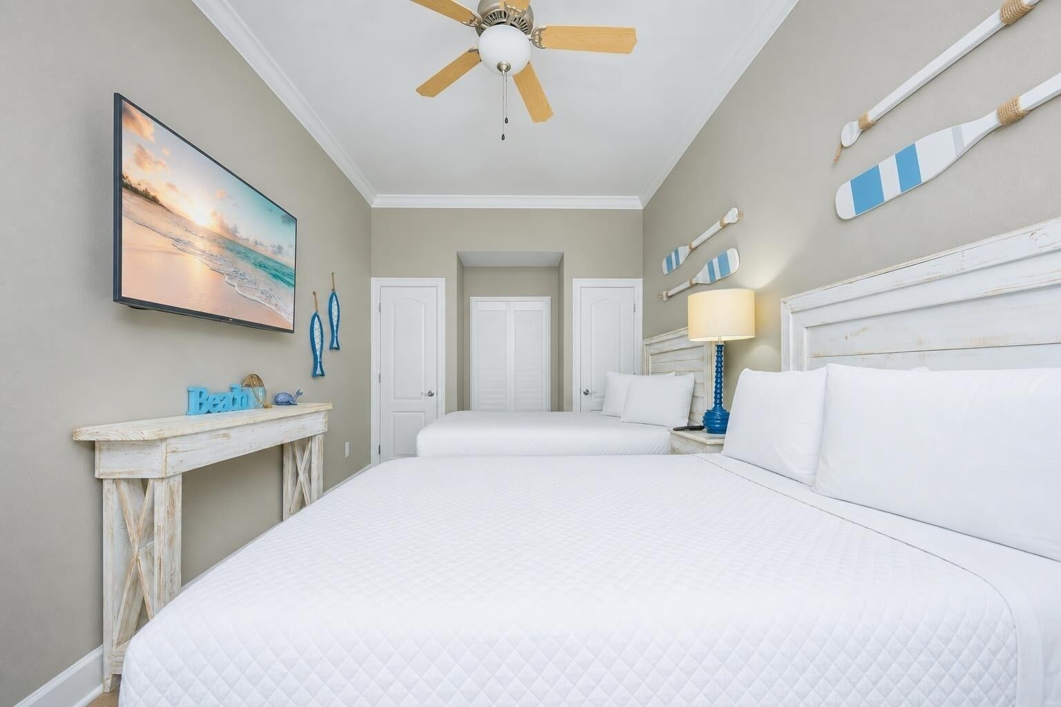 A hotel room with a bed, a ceiling fan, a painting, and a desk with a lamp.