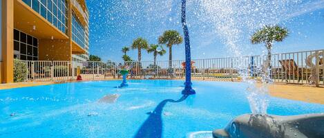 A pool area with a dolphin statue, a fountain, and a building with large windows.