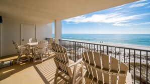 A balcony with a view of the beach, furnished with chairs and a table.