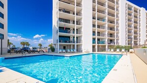A swimming pool with a clear blue water surface, surrounded by a white building with balconies.