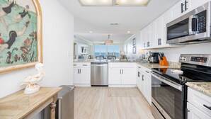 A modern kitchen with white cabinets, stainless steel appliances, and a large window providing a view of the outdoors.