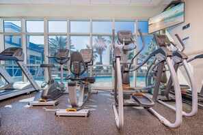 Un gimnasio con cintas de correr, elípticas y una piscina visibles a través de amplias ventanas.