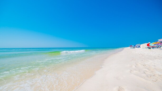 Ein Strand mit klarem türkisblauem Wasser, weißem Sand und bunten Sonnenschirmen.