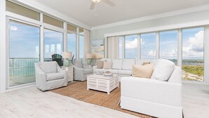 A spacious living room with a large window overlooking a scenic view, a white sofa, a coffee table, and a side table with decorative items. - Phoenix Gulf Towers 1101 4 Bedroom Condo (Orange Beach)