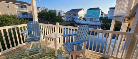 A wooden deck with two Adirondack chairs and a small table, overlooking a residential area with houses and a body of water.