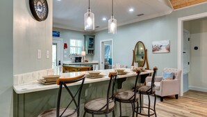A modern kitchen with a bar area, pendant lights, and a dining area with a white chair and bar stools.